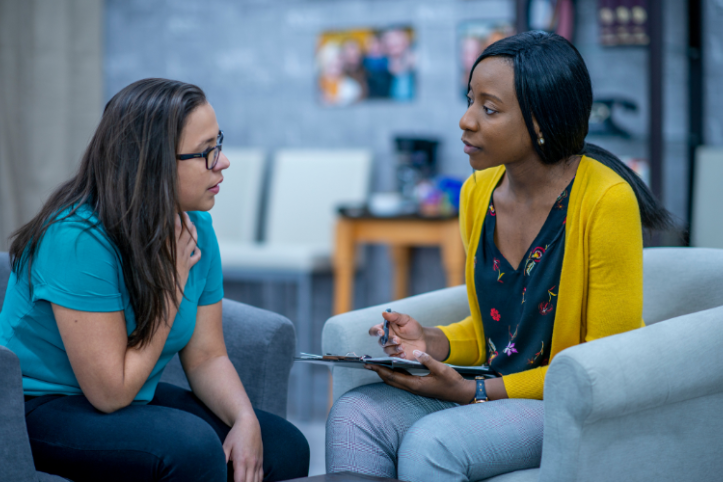 Two women talking to eachother. The woman on the right is taking notes of what's being said.