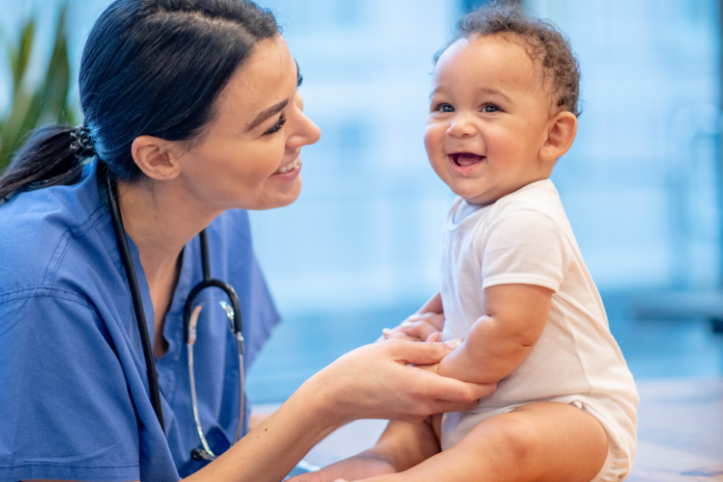 A female nurse holding a baby's hands as they both smile.