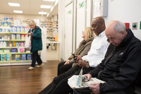 Three people sat waiting in a pharmacy