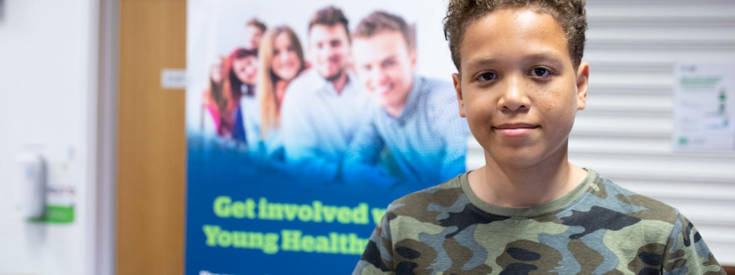 Young boy standing in front of a Healthwatch banner