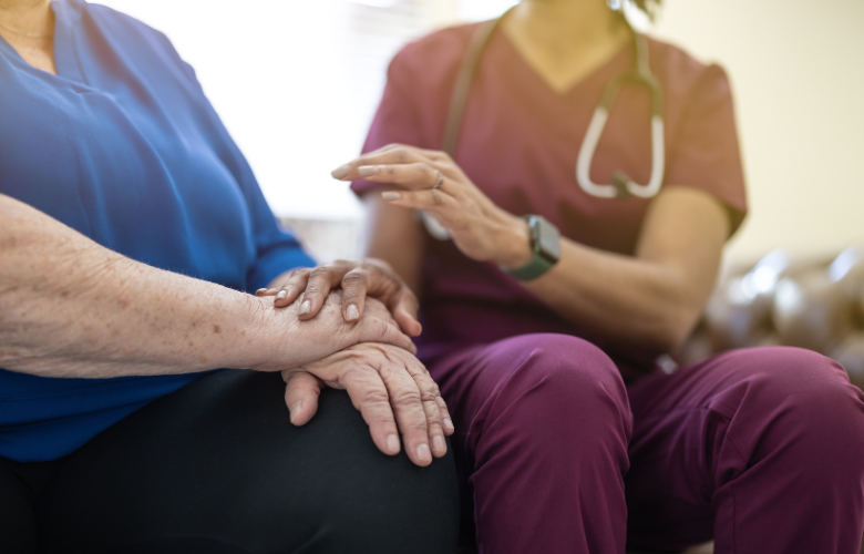 A hospice nurse in a purple uniform comforting an elderly person.